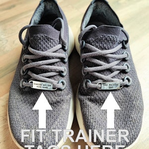 May include: A pair of gray athletic shoes with silver shoe laces and two silver metal tags on the laces. The tag on the left shoe says "Zombies eat the slow ones!" and the tag on the right shoe says "The walking Dad".