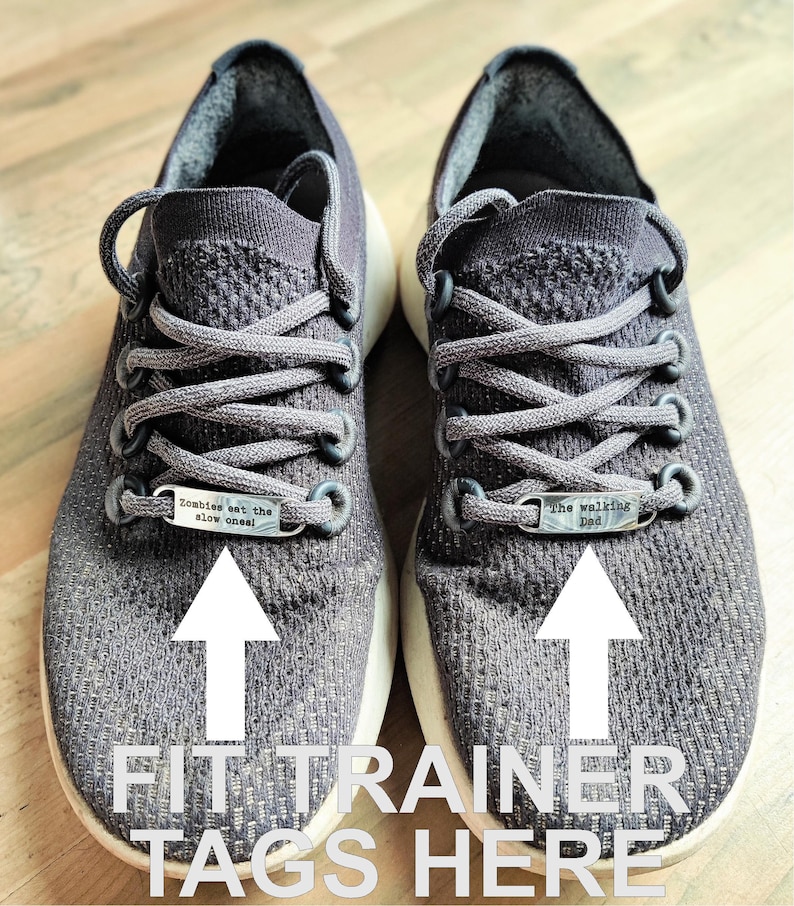 May include: A pair of gray athletic shoes with silver shoe laces and two silver metal tags on the laces. The tag on the left shoe says "Zombies eat the slow ones!" and the tag on the right shoe says "The walking Dad".