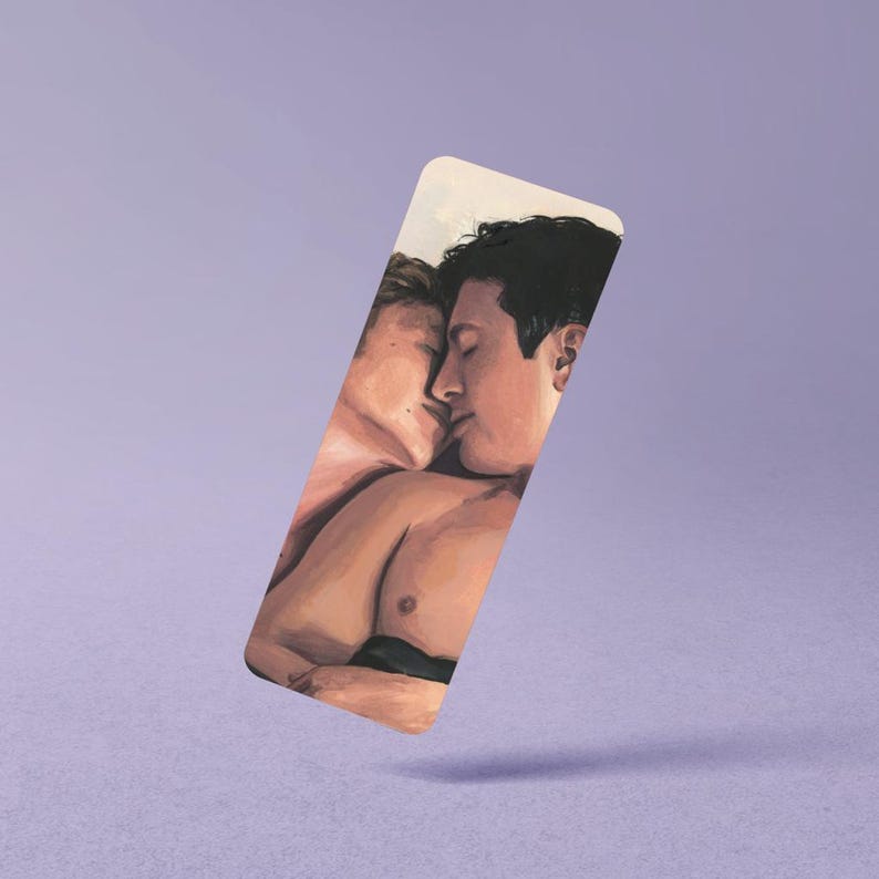 May include: A rectangular bookmark featuring a digital illustration of two individuals with short dark hair in a close, intimate embrace. The artwork uses warm skin tones and soft lighting to depict the figures from the chest up against a light background.