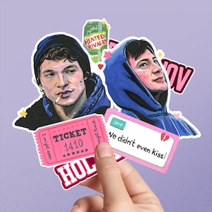 以下が含まれることがあります： パーカーを着た2人のイラスト、HEATED RIVALRYと書かれた緑色のソーダ缶、TICKET 1410と書かれたピンクのチケット、Jane We didn't even kissというテキストと壊れたハートのアイコンが描かれた白い長方形のステッカーを含むステッカーのコレクション。