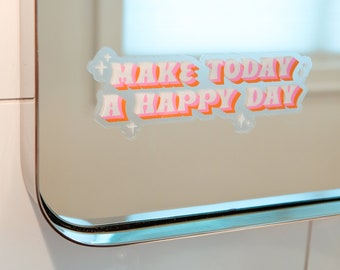 May include: A clear sticker with the text "MAKE TODAY A HAPPY DAY" in a retro font. The text is in white, pink, and orange, with a light blue outline and star accents. The sticker is adhered to a mirror.