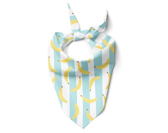 May include: A triangular bandana featuring a repeating pattern of yellow bananas on a light blue and white striped background. The bandana is tied at the top, showcasing the playful design. This accessory is suitable for pets.