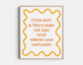 May include: A framed art print with a white background and orange text. The text includes the words "STRAW HATS, AL FRESCO DINING, TAN LINES, ROSÉ, WINDOWS DOWN, SUNFLOWERS." The text is surrounded by an orange wavy border. The frame is a light wood color.