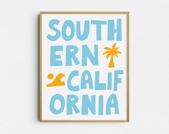 May include: A framed print with the words "SOUTHERN CALIFORNIA" in blue, stylized letters. An orange wave and palm tree graphic are included. The print has a light wood frame and is displayed against a white wall.