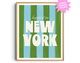 May include: A framed art print with a light wood frame. The artwork features vertical stripes in green and light blue. The words "happiest in NEW YORK" are in large white letters. A pink starburst graphic says "COMES IN MORE COLORS".