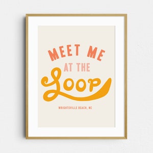 May include: A framed art print with the words "MEET ME AT THE LOOP" in coral and orange lettering. The text "WRIGHTSVILLE BEACH, NC" is printed below in a smaller font. The artwork is set against a cream background.