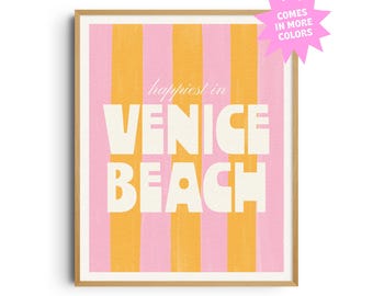 May include: A framed art print with a pink and orange striped background. The words "happiest in VENICE BEACH" are printed in large white letters. A pink starburst graphic indicates the print is available in more colors.