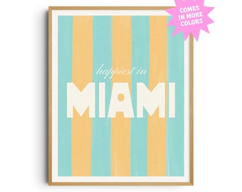 May include: Framed art print with a vertical striped pattern in light blue and yellow. The words "happiest in MIAMI" are displayed in white, bold font. A pink starburst graphic in the upper right corner reads "COMES IN MORE COLORS".