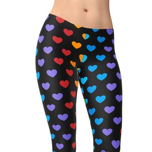 May include: Black leggings with a rainbow heart pattern. The hearts are in a repeating pattern and are arranged in a vertical line. The leggings are full length and are shown on a model.