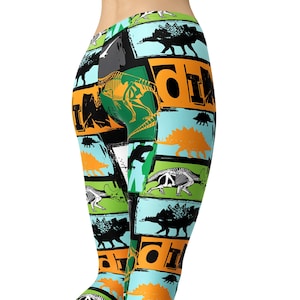 Könnte beinhalten: Eine blaue, grüne, orange und schwarze Leggings mit einem Dinosaurier-Druck. Die Leggings hat ein sich wiederholendes Muster aus Dinosauriern, Knochen und dem Wort "Dino".