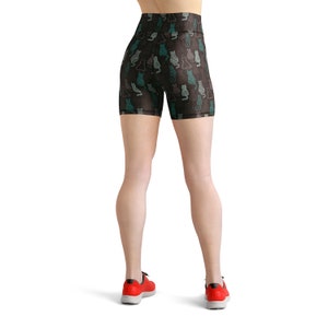 May include: Black high-waisted athletic shorts with a repeating pattern of teal and gray cat silhouettes. The shorts are worn with red athletic shoes. The overall theme is fitness and activewear.