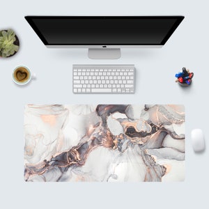 May include: A white desk mat with a marble pattern featuring swirls of gray, black, and gold. The mat is designed to protect a desk surface from scratches and wear.