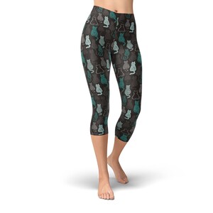 May include: Cropped leggings with a repeating pattern of stylized cats in teal, gray, and white on a dark gray background. The leggings are knee-length and form-fitting, suitable for athletic activities or casual wear.
