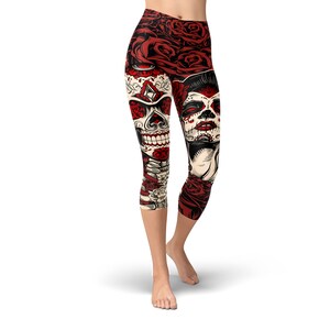 May include: Red, white, and black patterned leggings with a skull and sugar skull design. The leggings are cropped and have a floral pattern.