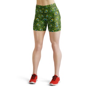 May include: Green and blue athletic shorts with a peacock feather pattern. The shorts are worn by a person with bare legs and red sneakers.