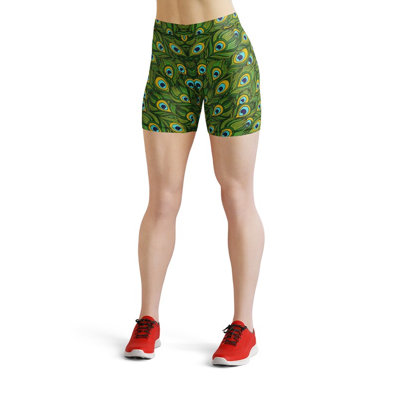 May include: Green and blue athletic shorts with a peacock feather pattern. The shorts are worn by a person with bare legs and red sneakers.