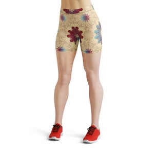 K&ouml;nnte beinhalten: Eine kurze Sporthose mit cremefarbenem Hintergrund und einem bunten Blumenmuster. Die Shorts werden von einer Person mit nackten Beinen und roten Turnschuhen getragen.