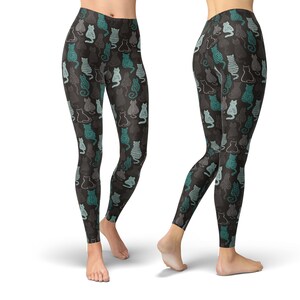 May include: Black leggings with a repeating pattern of stylized cats in teal, gray, and white. The cats have various designs, including stripes and solid outlines. The leggings are form-fitting and reach the ankles.