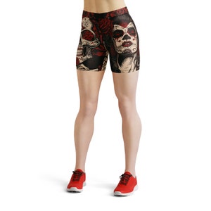 May include: Black and red athletic shorts with a skull and sugar skull design. The shorts are worn by a person with red athletic shoes.