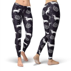 May include: Black leggings with a white print of dachshunds wearing astronaut helmets and floating in space. The print also includes white circles with a textured pattern.