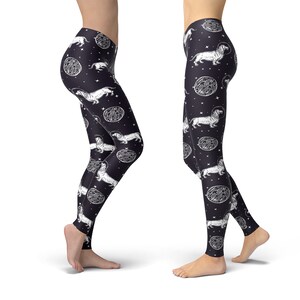 May include: Black leggings with a white print of dachshunds wearing astronaut helmets and floating in space. The print also includes white circles with a textured pattern.