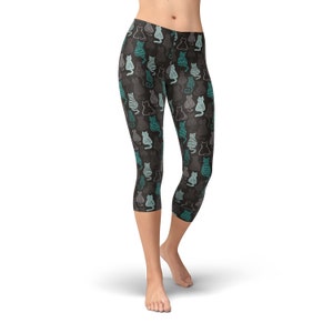 May include: Cropped leggings with a repeating pattern of stylized cats in teal, gray, and white on a dark gray background. The leggings are mid-calf length and form-fitting, suitable for athletic or casual wear.