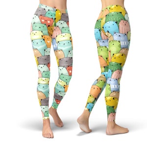 May include: Colorful leggings with a pattern of cartoon cats in various colors and poses. The leggings are shown on two models, one standing with their legs apart and the other standing with their legs crossed.