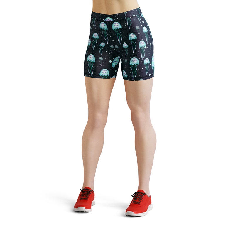 May include: Black athletic shorts with a jellyfish print. The shorts have a high waist and a fitted silhouette. The jellyfish are blue and green with pink accents. The background is black with white stars.