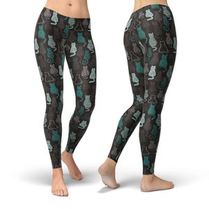 May include: Black leggings with a repeating pattern of stylized cats in teal, gray, and white. The cats have various designs, including stripes and solid fills. The leggings are form-fitting and made of a soft material.