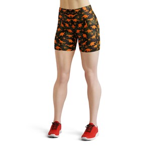 May include: Black and green athletic shorts with an orange dinosaur print. The shorts are worn by a person with red sneakers.
