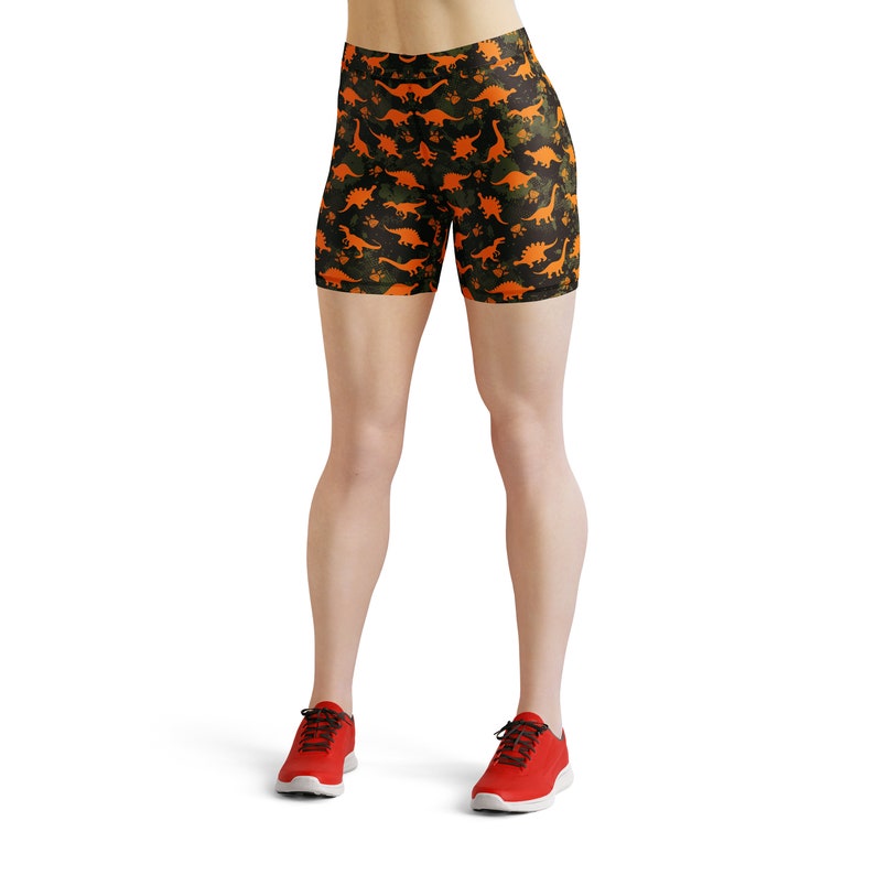 May include: Black and green athletic shorts with an orange dinosaur print. The shorts are worn by a person with red sneakers.