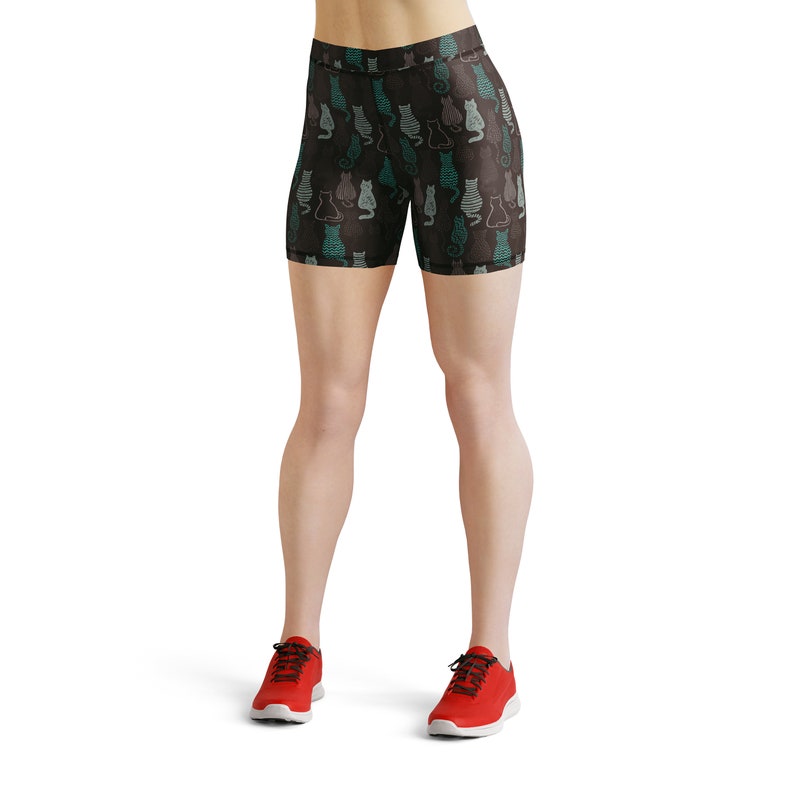 May include: Black athletic shorts with a repeating pattern of stylized cats in teal, gray, and white. The shorts are worn with red athletic shoes with black laces.
