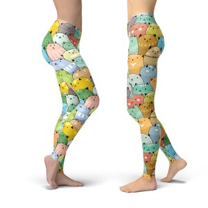 May include: A pair of colorful leggings with a pattern of cartoon cats in various colors and poses. The leggings are shown on two models, one wearing the leggings on the left leg and the other wearing the leggings on the right leg.