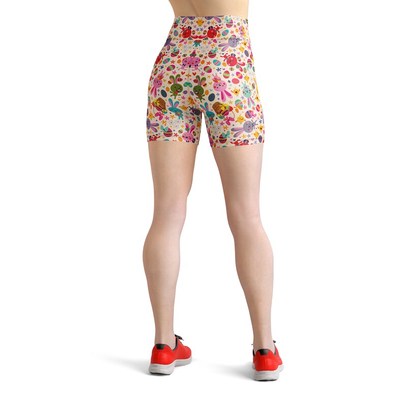 May include: A pair of white athletic shorts with a colourful Easter-themed pattern featuring bunnies, eggs, and flowers. The shorts have a high waist and are made of a stretchy, comfortable fabric.