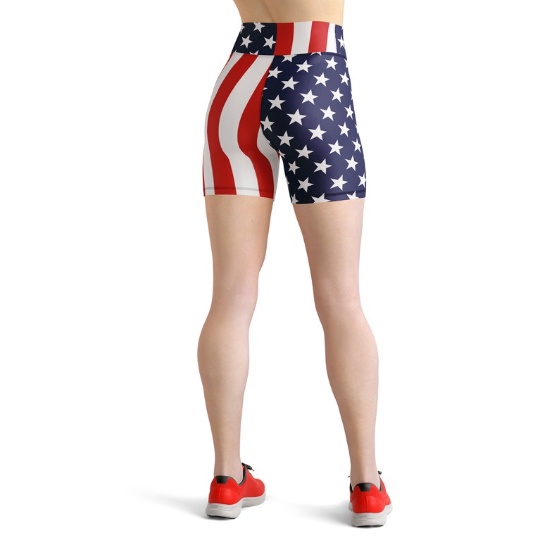 May include: A pair of athletic shorts with a red, white, and blue American flag design. The shorts are worn by a person with red sneakers.