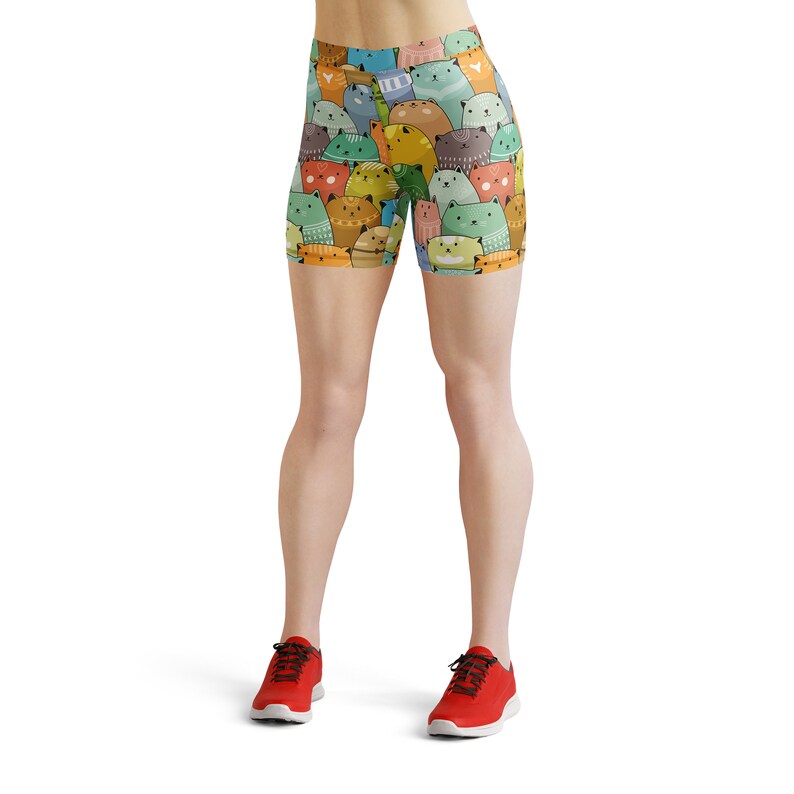 May include: A pair of athletic shorts with a colorful print of cartoon cats. The shorts are a bright yellow, green, blue, and orange. The model is wearing red athletic shoes.