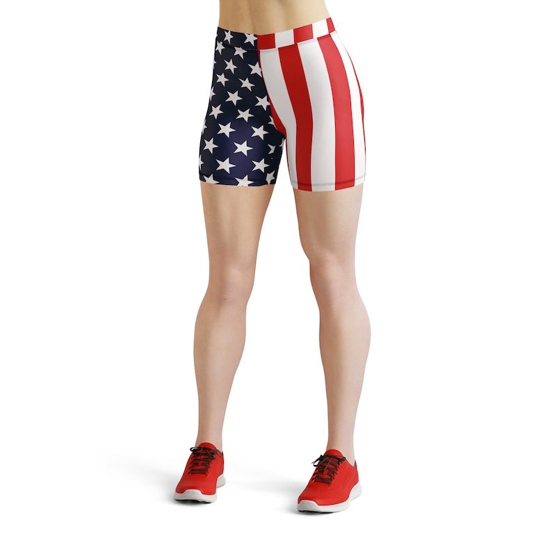 May include: A pair of athletic shorts with a red, white, and blue American flag design. The shorts are worn by a person with bare legs and red athletic shoes.