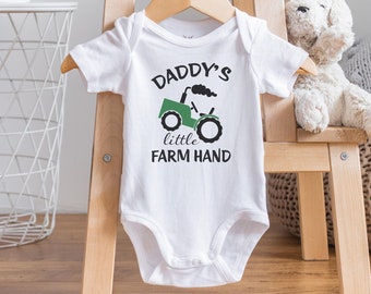 May include: White baby onesie with a green tractor and the text "Daddy's little farm hand".