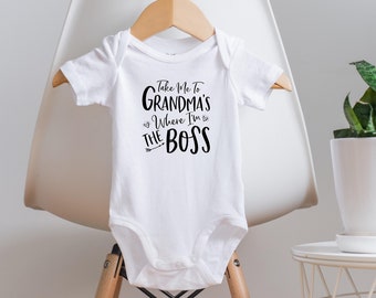 Könnte beinhalten: Weißer Baby-Strampler mit schwarzem Text, der "Take Me To Grandma's Where I'm The Boss" lautet, mit einem Pfeil, der nach rechts zeigt.