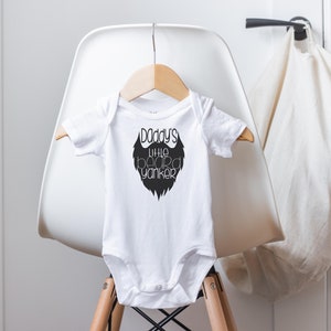 May include: White baby onesie with a black graphic of a beard and the text "Daddy's little beard yankers".