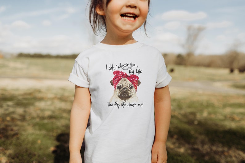 Peut inclure: Un t-shirt blanc avec un graphique d'un carlin portant un bandana rouge et blanc. Le texte sur le t-shirt est "Je n'ai pas choisi la vie du carlin. La vie du carlin m'a choisi !"