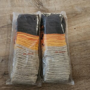 May include: Two pairs of folded socks packaged in clear plastic sleeves. Each pair features a color-blocked design with a dark charcoal top, followed by bands of orange, yellow, and a light beige base. The text 975 3015-00 is printed in red.