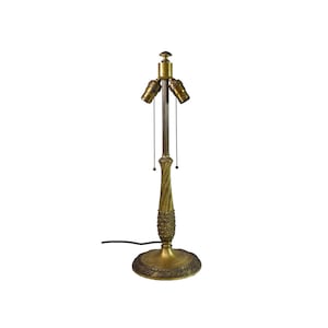 May include: A gold-toned metal lamp base with a decorative, twisted design and a round base. The lamp has two sockets with pull chains.