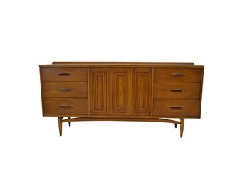 May include: A mid-century modern dresser with six drawers and two cabinet doors. The dresser is made of wood and has a light brown finish. The drawers have brass pulls. The cabinet doors have a raised panel design.