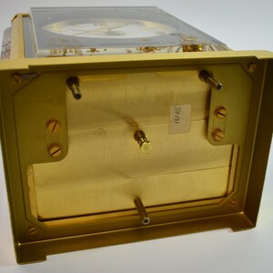 May include: The bottom of a gold-colored clock with a clear glass top. The clock has a label on the bottom that reads "310/191".