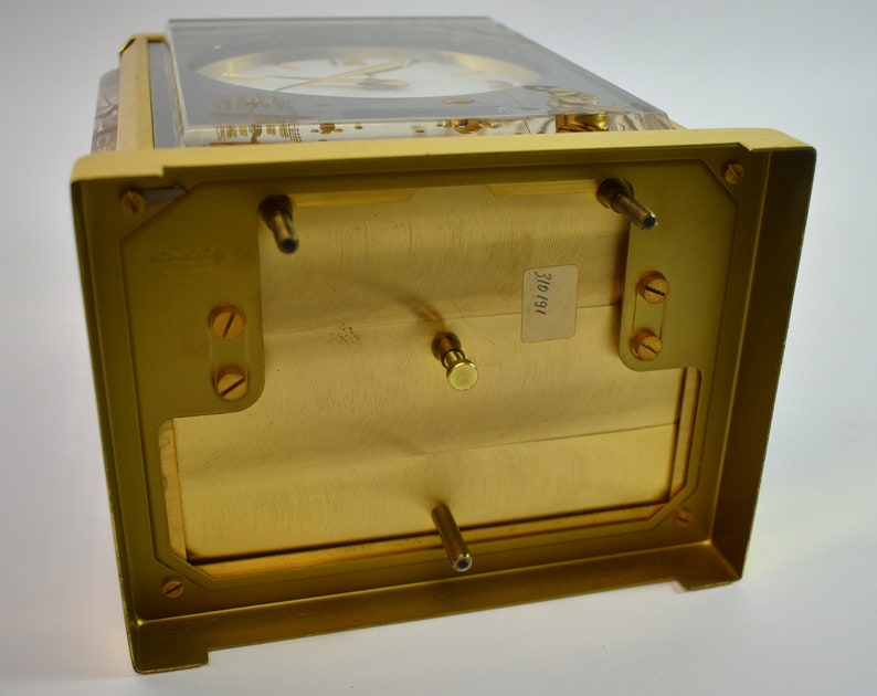 May include: The bottom of a gold-colored clock with a clear glass top. The clock has a label on the bottom that reads "310/191".