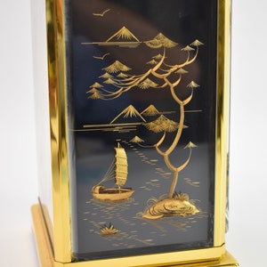 May include: A gold-framed box with a black background and a gold-colored scene of a sailboat on a lake with mountains and trees in the background.
