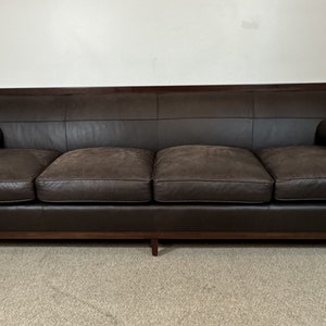 May include: A brown leather sofa with a dark wood frame and two pillows. The sofa has a tufted design and is in good condition.