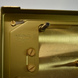 May include: Close-up of the back of a gold-colored watch movement. The movement is engraved with the text "Le Coultre & Cie Metal Caliber 15045 Swiss".
