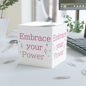 May include: White cube with the text "Embrace your Power" on two sides in pink lettering with silver glitter accents. The cube is sitting on a white surface.